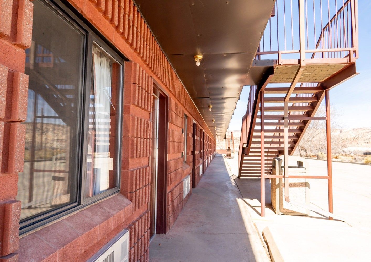 Outdoor motel corridor with brick walls, windows, and a metal staircase at the end
