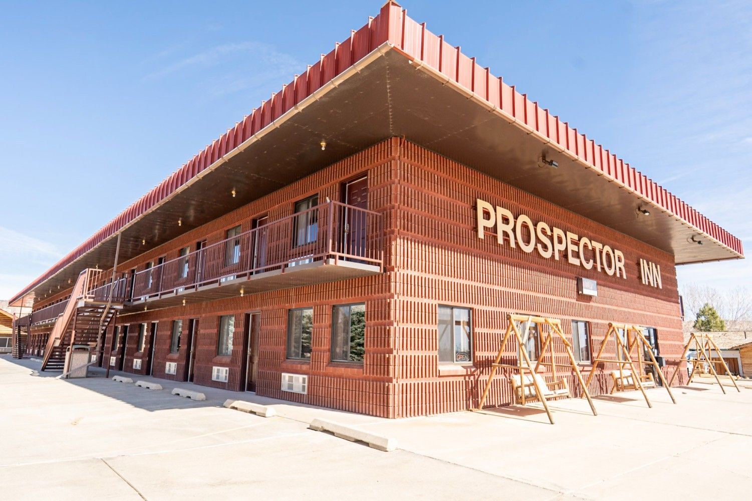 Brick Prospector building with wooden trim and red roof overhang on a sunny street corner