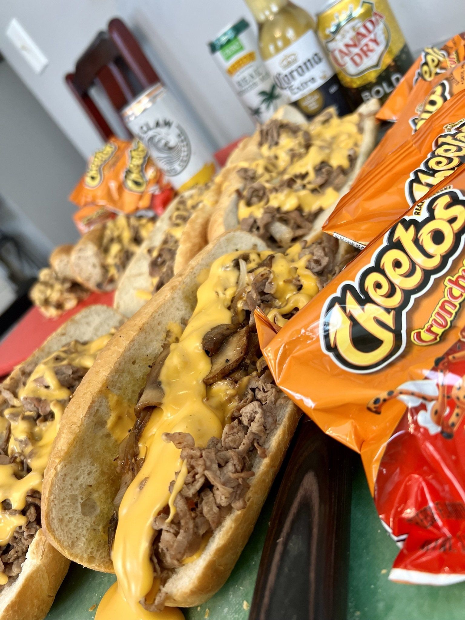 Philly cheesesteaks, Cheetos, and drinks on a table.