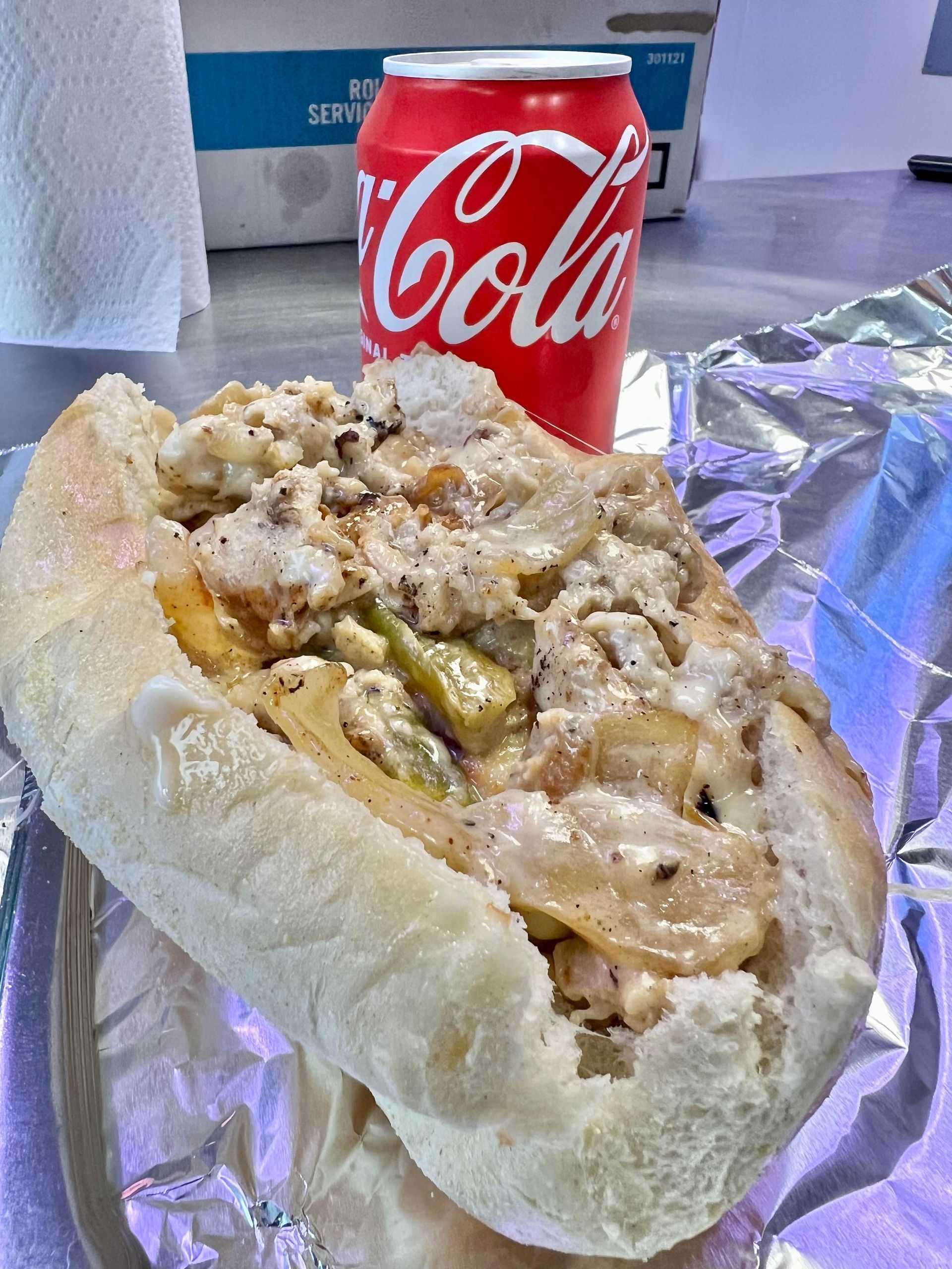 Cheesesteak sandwich with Coca-Cola can on foil.