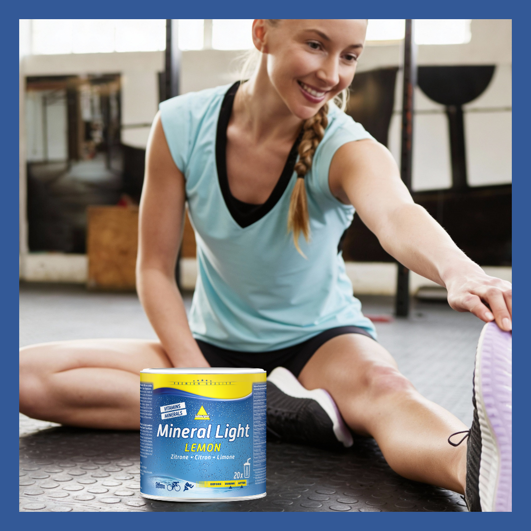 Una donna fa stretching, tenendo in mano un contenitore di Mineral Light in palestra. Sorride e indossa abbigliamento sportivo.