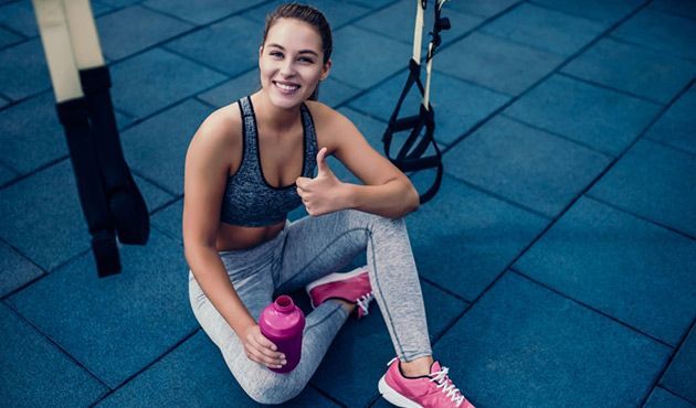 Donna in abbigliamento sportivo che alza il pollice e tiene in mano una bottiglia d'acqua,