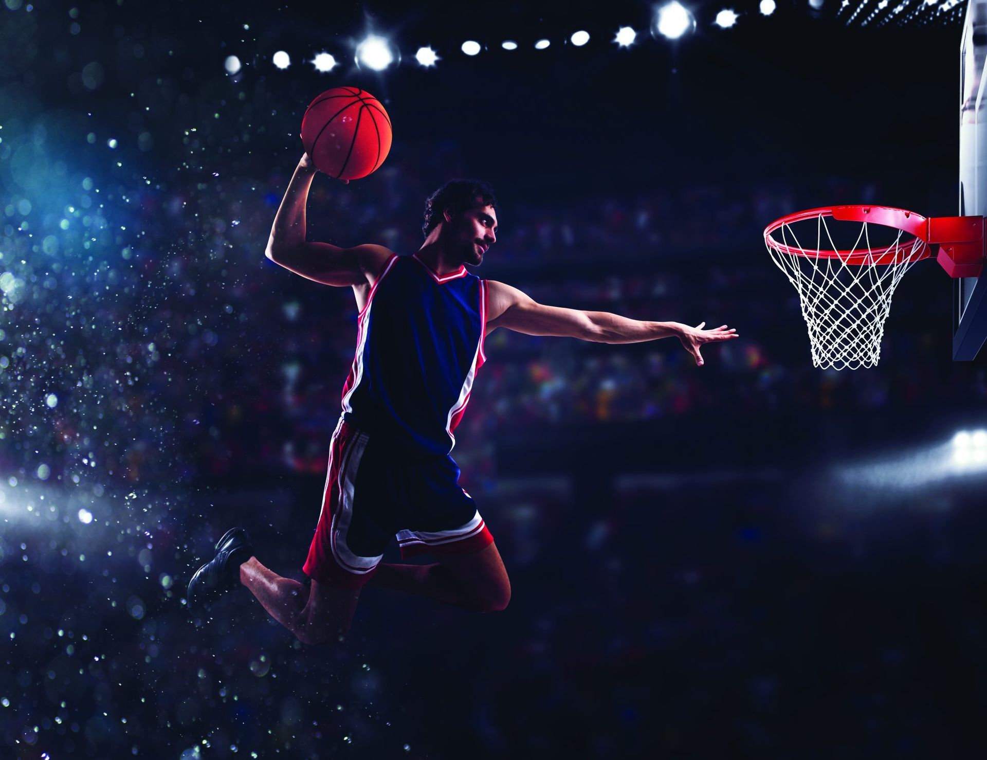 Un giocatore di basket schiaccia con la palla in mano in un'arena ben illuminata, con la folla sullo sfondo.