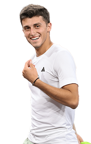 Giocatore di tennis sorridente con maglietta bianca, braccio alzato, campo verde visibile.