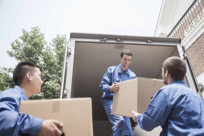three men are loading boxes into a moving truck .