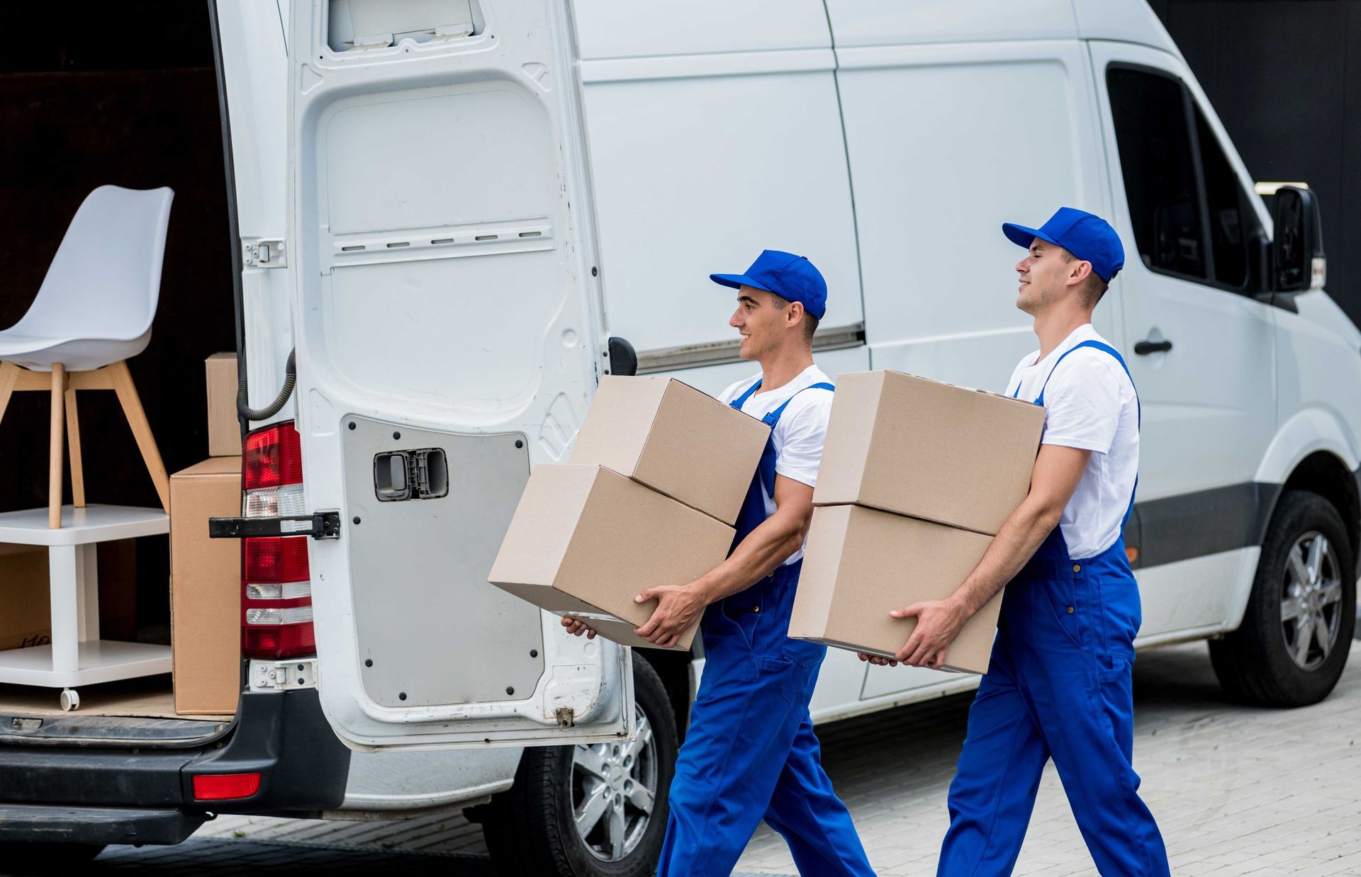 two movers are carrying boxes out of a van .