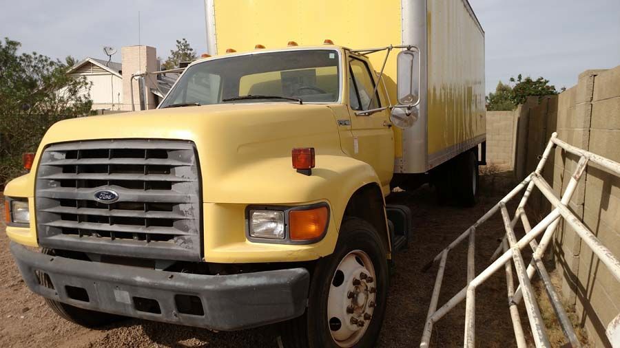 a yellow truck is parked next to a white trailer .