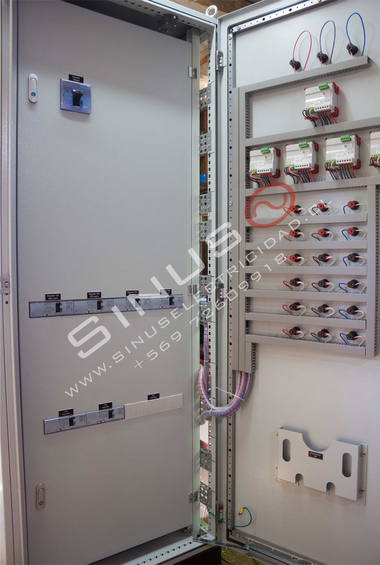 Panel de control eléctrico abierto con cableado, interruptores y componentes del circuito dentro de un armario metálico.