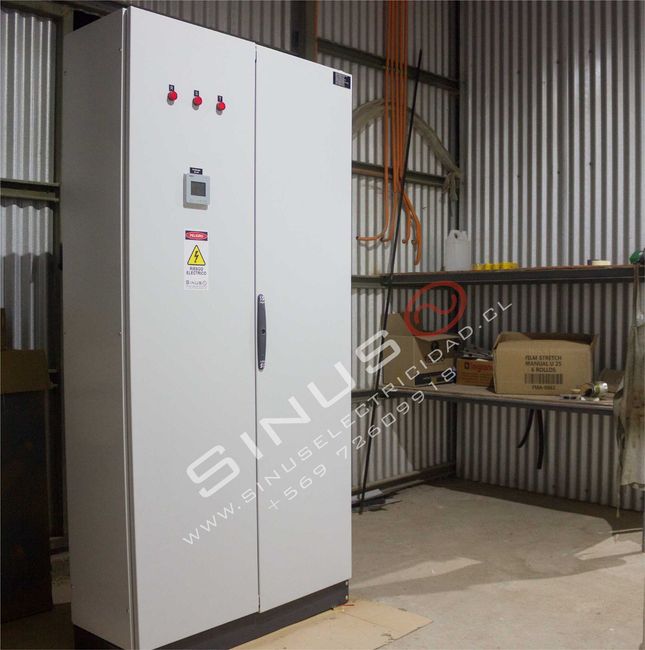 Armario de control eléctrico industrial blanco en un taller de chapa ondulada, con estantes y herramientas cerca.