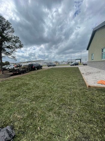 Lawn in front of a building with vehicles in the distance under a cloudy sky.