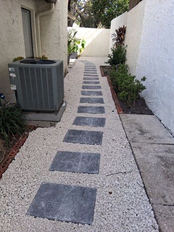 Pathway with gray stepping stones, bordered by white gravel and walls.