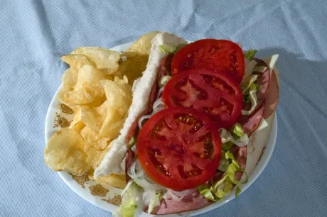 A plate containing a deli sandwich topped with fresh tomato slices and a side of potato chips.