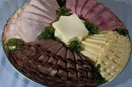 A round platter filled with sections of sliced turkey, ham, roast beef, and two types of cheese, garnished with parsley.