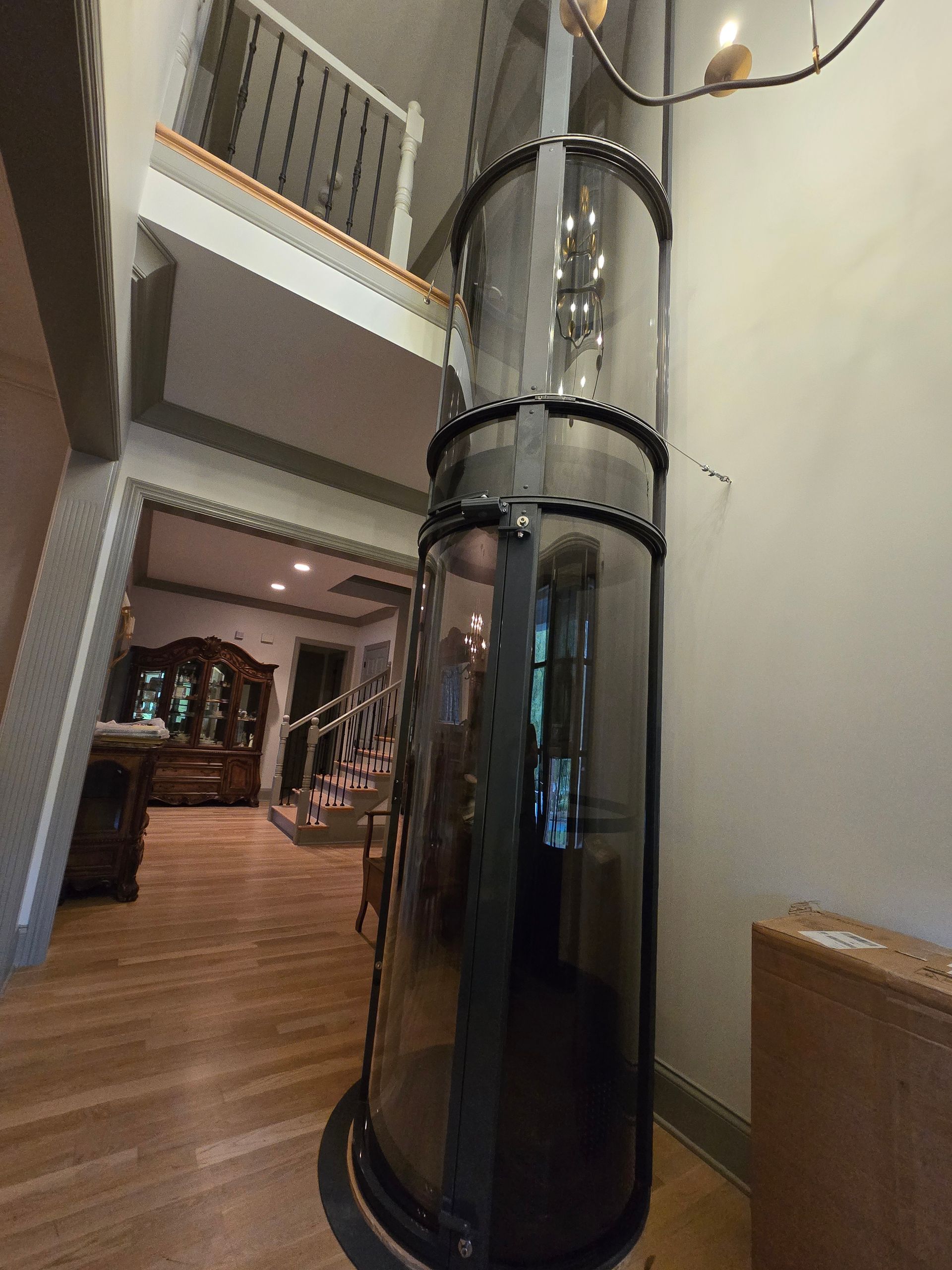 A glass elevator is in the middle of a room in a house.