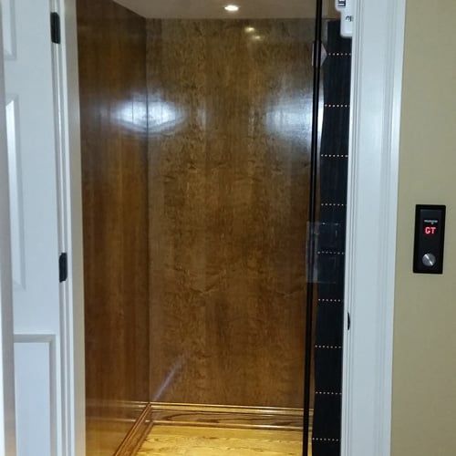An elevator with a wooden wall and a glass door.