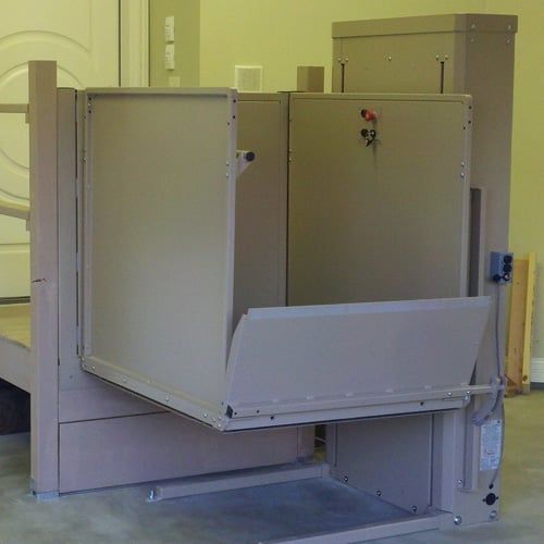 A wheelchair lift is sitting in a garage with the door open.