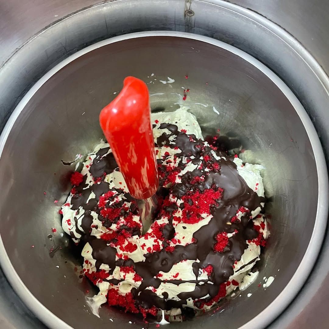 Gelatiera con gelato color menta, granella rossa e sciroppo al cioccolato. Pala rossa al centro.