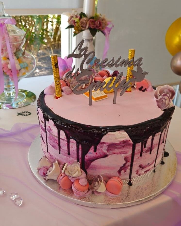 Torta glassata rosa con gocce di cioccolato fondente, guarnita con decorazioni e un cake topper con la scritta "Cresima di Emily".