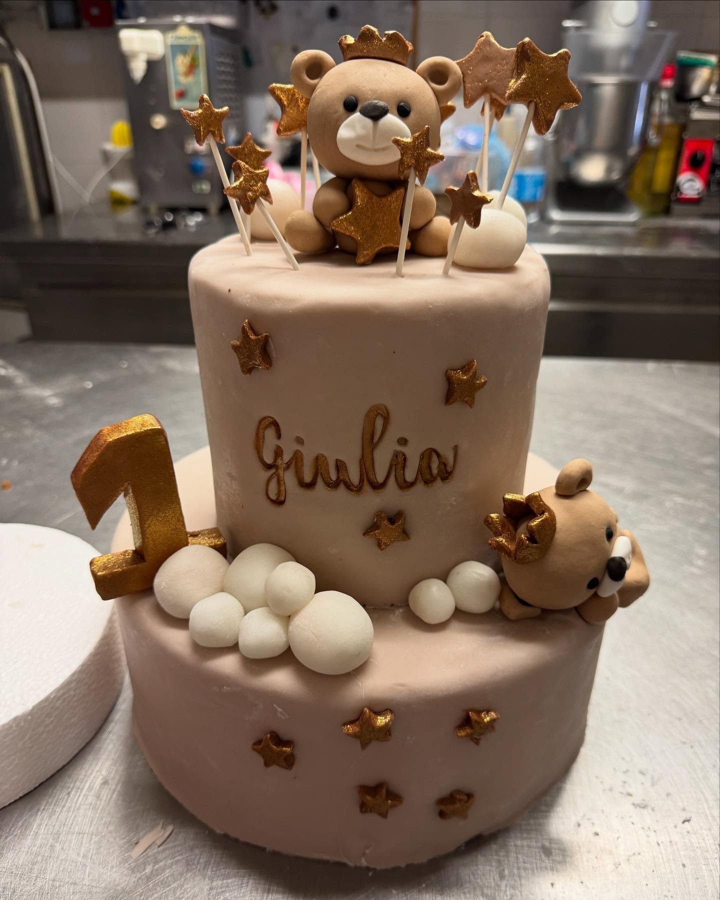 Torta di compleanno a due piani con decorazione a forma di orsetto, stelle dorate e il nome "Giulia".