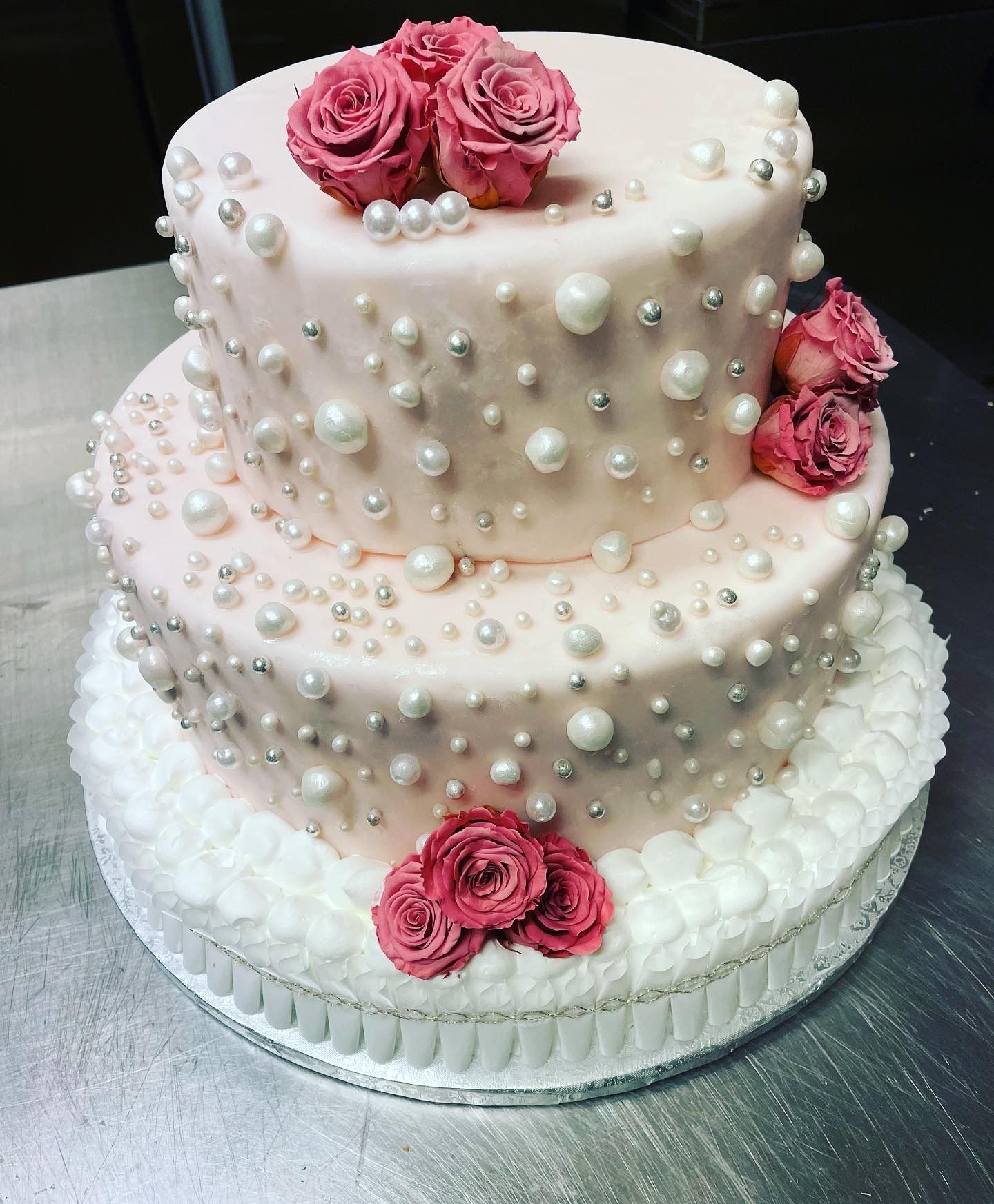 Torta rosa a due piani decorata con perle, rose e glassa bianca.