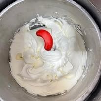 La crema bianca viene mescolata in una ciotola di metallo con una spatola rossa.