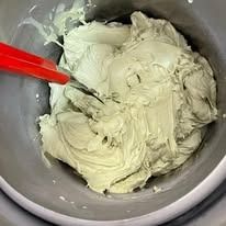 Glassa verde in una ciotola grigia mescolata con una spatola rossa.