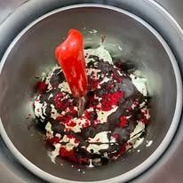 Primo piano del dessert in una ciotola di metallo con guarnizione rossa, colori chiari e scuri mescolati, un utensile rosso.