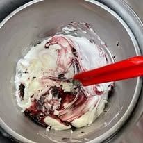 Glassa bianca e bordeaux in una ciotola di acciaio inossidabile, spatola rossa.