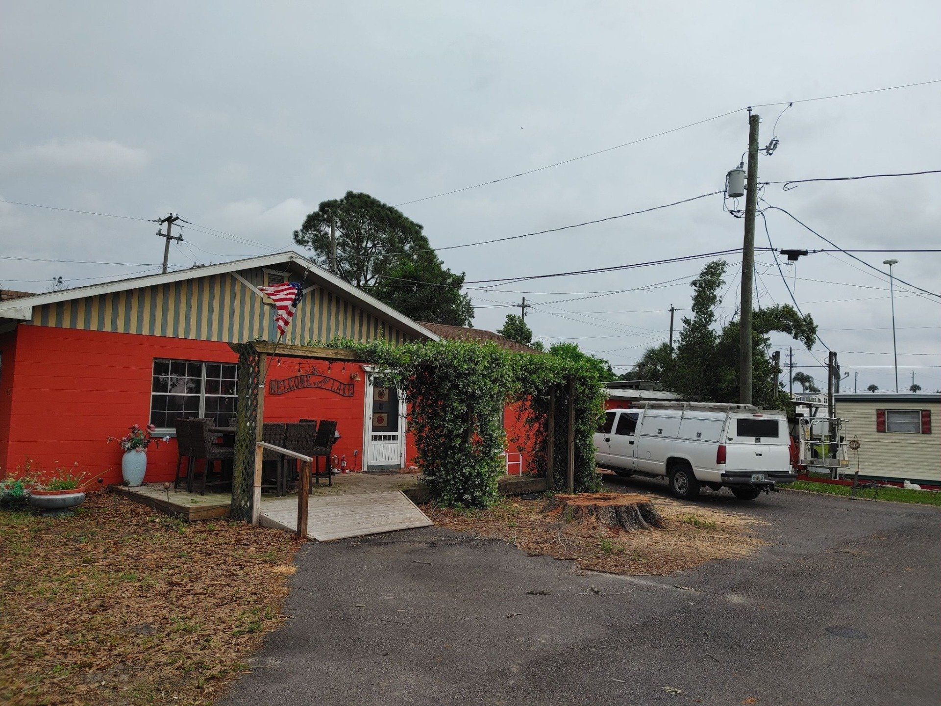 Red building with an entrance under a vine-covered trellis, a white van parked nearby, and power lines overhead.