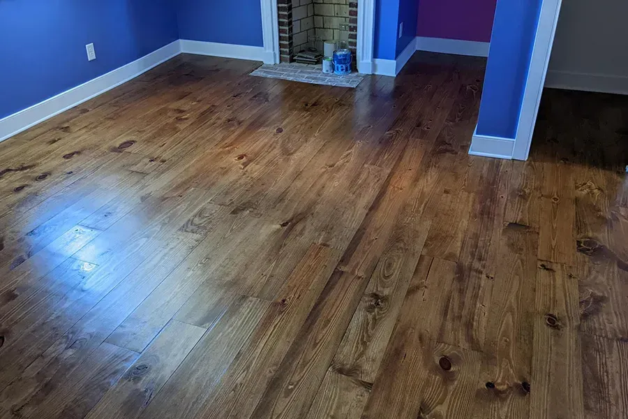 Hardwood floors with a medium brown stain in a room with blue walls and white trim, near a fireplace.