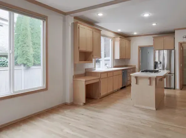 Light-filled kitchen with wooden cabinets, light hardwood floors, and stainless steel appliances. A large window offers an outdoor view.