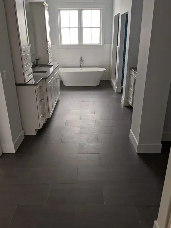 A luxurious bathroom with a dark wood floor, white cabinets, and a freestanding tub beneath a window.
