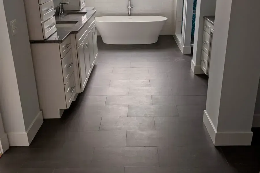 Dark wood-look tile flooring in a modern bathroom with white cabinets, a freestanding tub, and light gray walls.