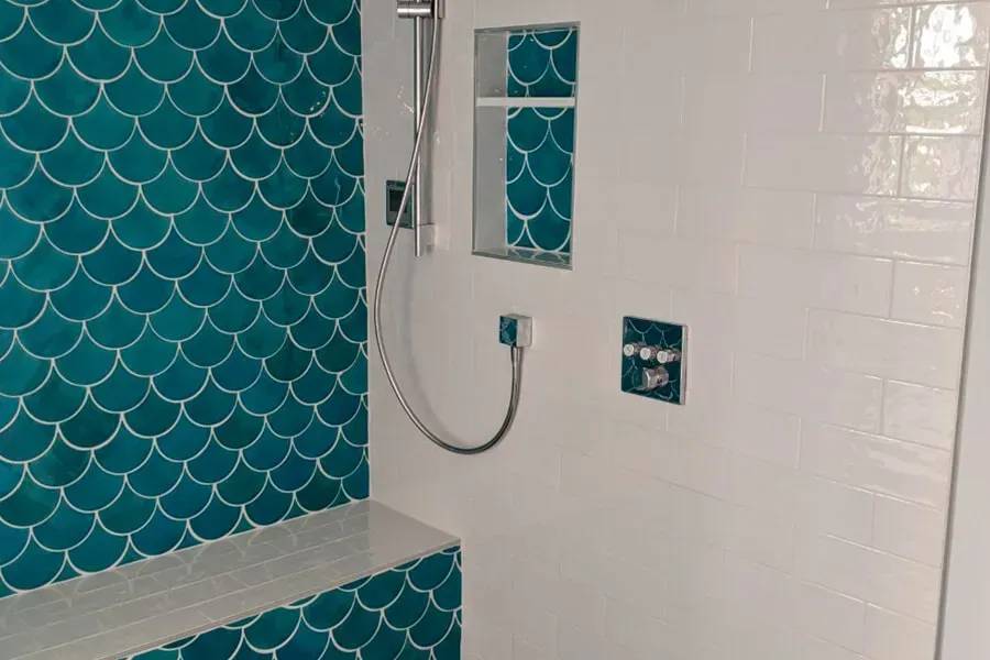Shower with teal fish-scale tile and white subway tile. Features a built-in bench and shower niche, with chrome fixtures.