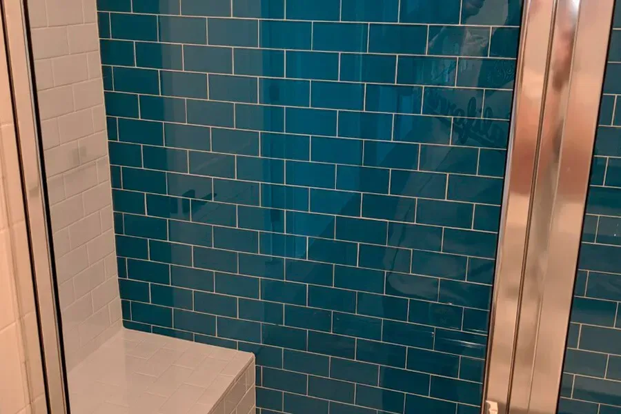 Blue tiled shower interior with a chrome shower door and white wall.
