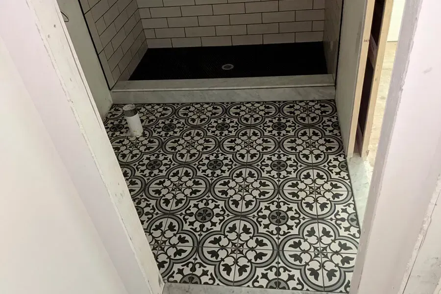 Bathroom with black and white patterned tile floor and a shower with a black base and white brick-like tiles.