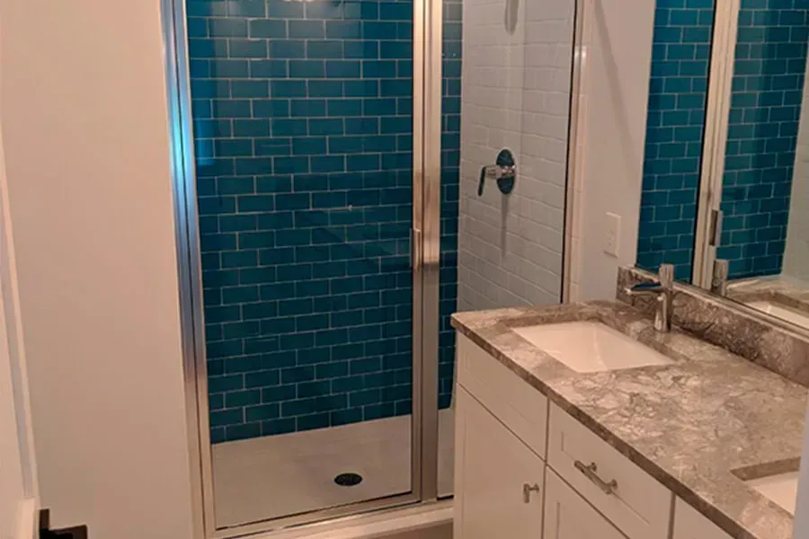 Bathroom with a teal tile shower, a white double vanity, and a grey countertop.