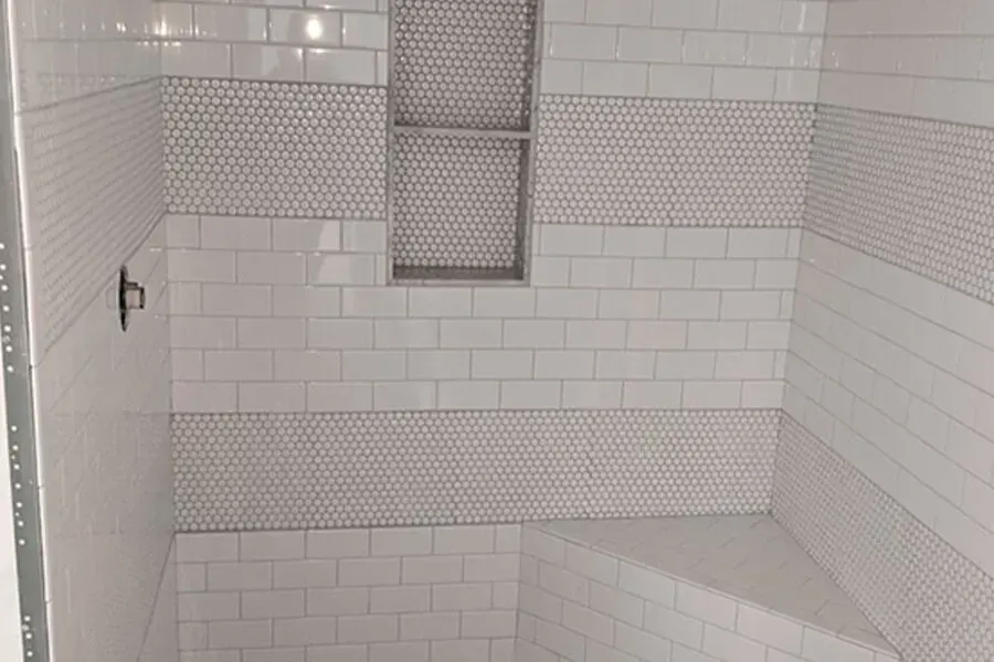White-tiled shower with a mosaic tile stripe and built-in niche. A corner bench is also tiled white.