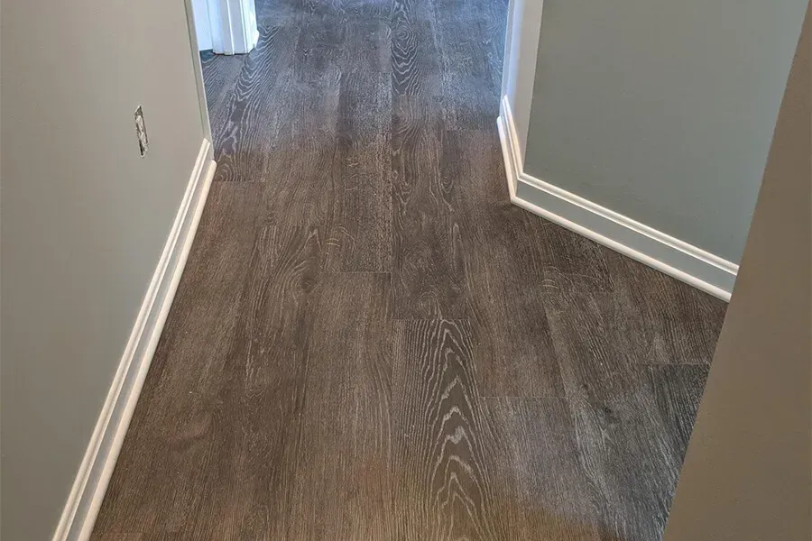 Dark wood-look flooring in a hallway with white trim and tan walls.