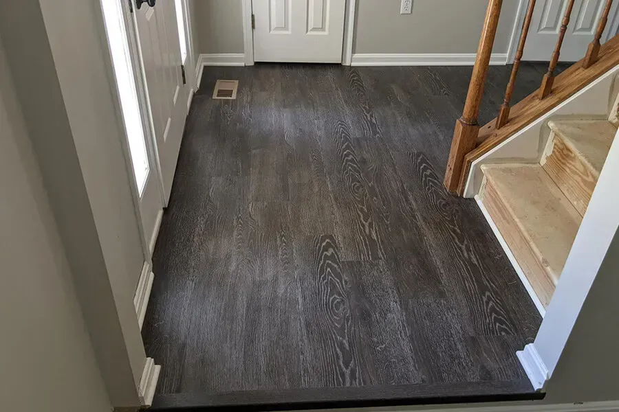 Dark wood flooring in an entryway with a white door, staircase, and gray walls.