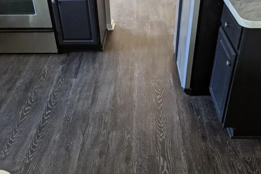Dark gray wood-look flooring in a kitchen. A cabinet and appliance are visible on either side.
