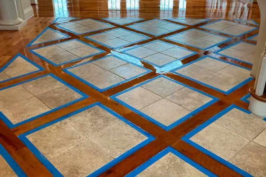 Tiled flooring design with beige squares bordered by blue tape, set against a dark wood floor with a glossy sheen.