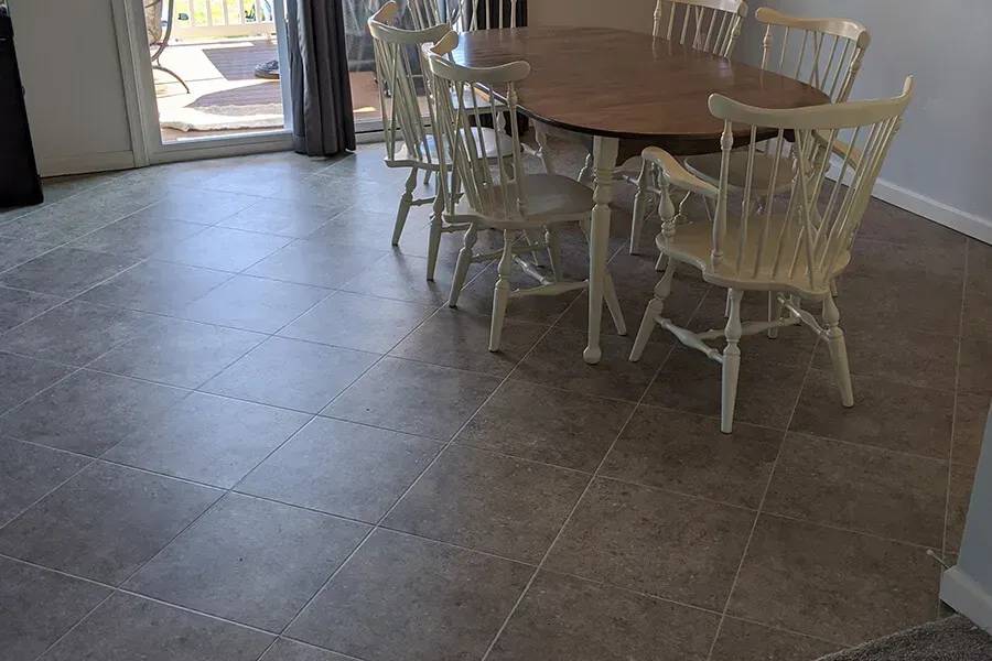 A dining room with a large oval table and six white wooden chairs on a tiled floor