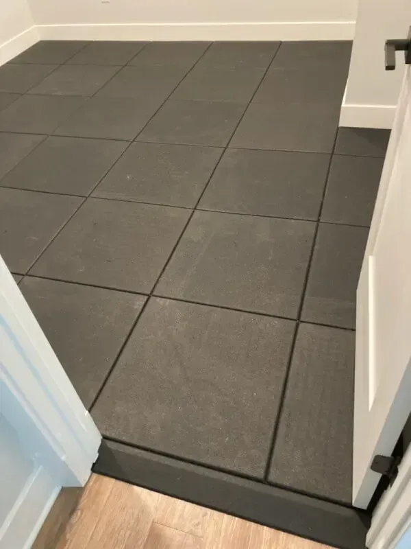 Room with dark gray rubber floor tiles, viewed from a doorway, with white trim on the walls and door frame.