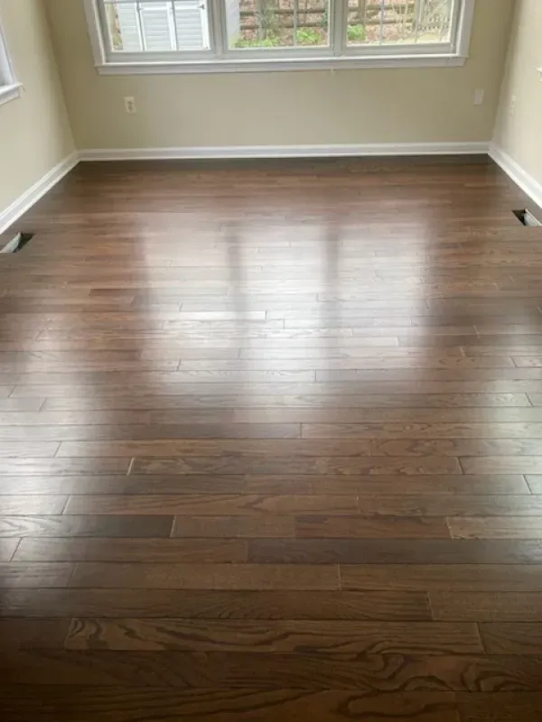 Dark brown hardwood floor in a room with white trim and a window, reflecting light.