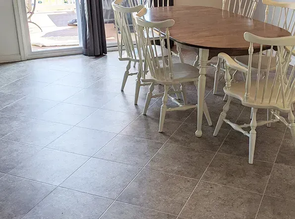 A dining room with a wooden table and white chairs on grey tiled flooring. A sliding door is visible in the background.