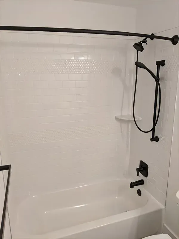 White bathroom with subway tile walls and black fixtures, including a showerhead, handheld shower, and faucet.