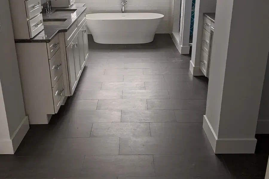 Dark tiled floor in a bathroom with white cabinets, a standalone tub, and white walls.
