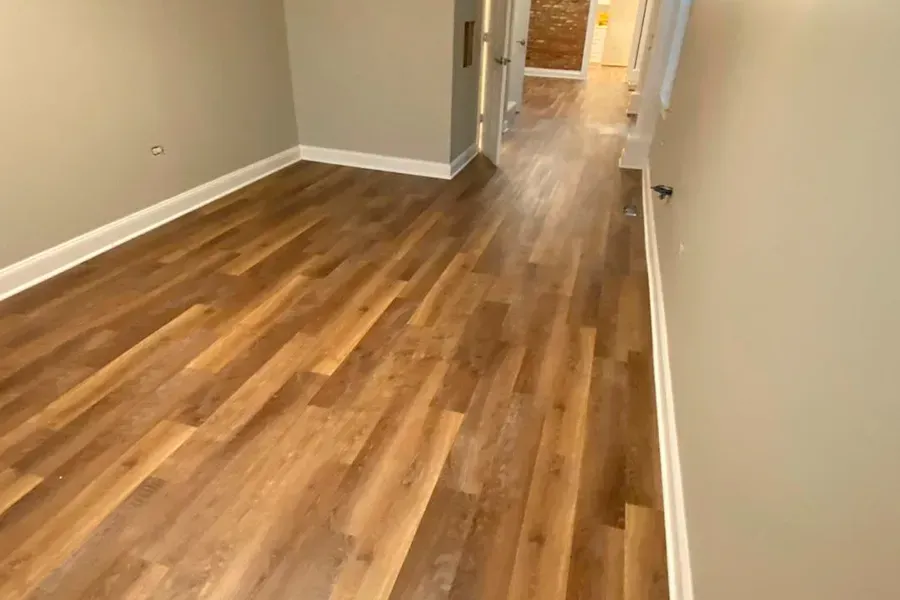 Wooden floor in a hallway with light-colored walls and white trim. A doorway is visible at the end of the hallway.