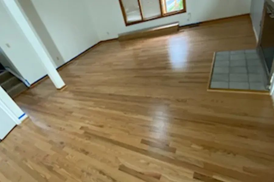 Hardwood flooring in a room with a fireplace and windows. The floor has a glossy finish.